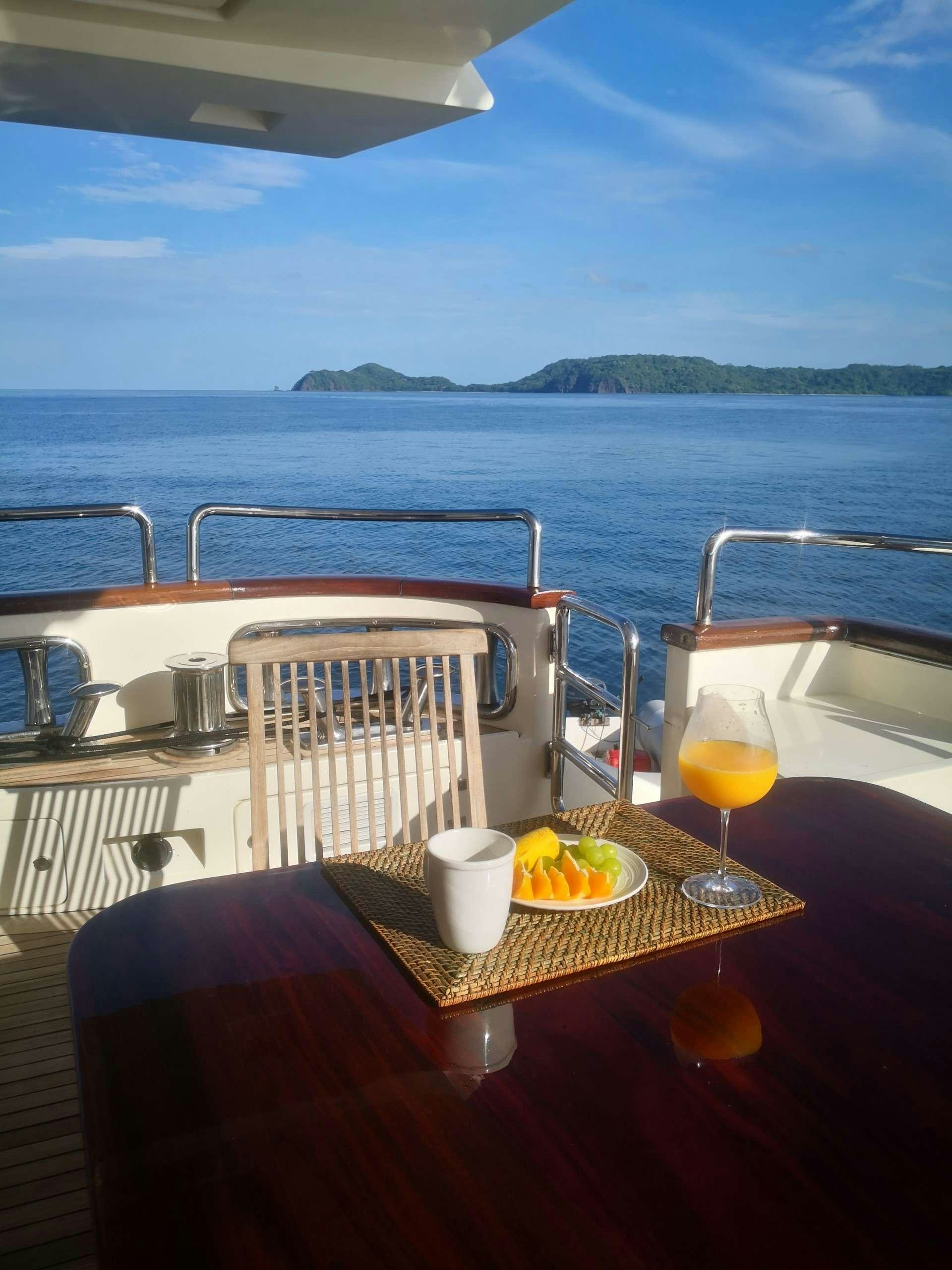 a table with a glass of juice on it and a view of the ocean and mountains in the aboard CAMY ED Yacht for Charter