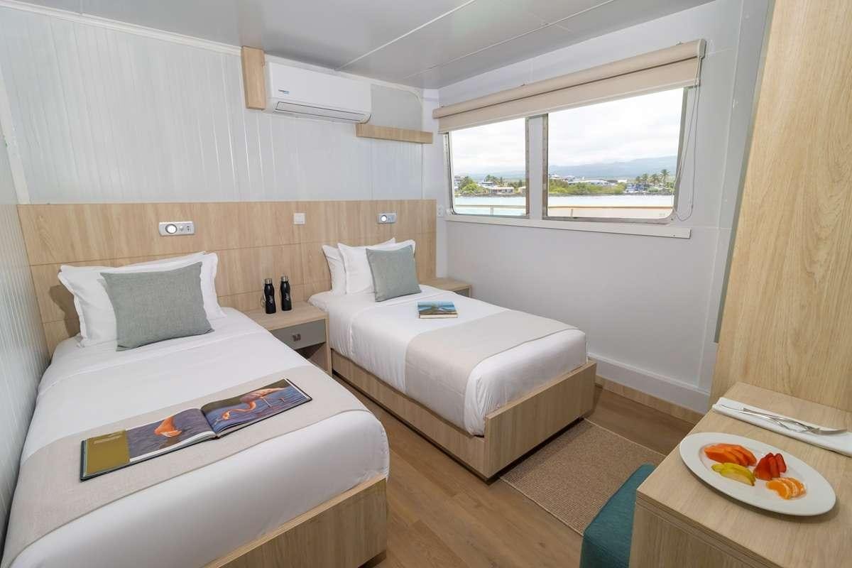 a room with two beds and a table aboard GALAPAGOS ANGEL Yacht for Charter