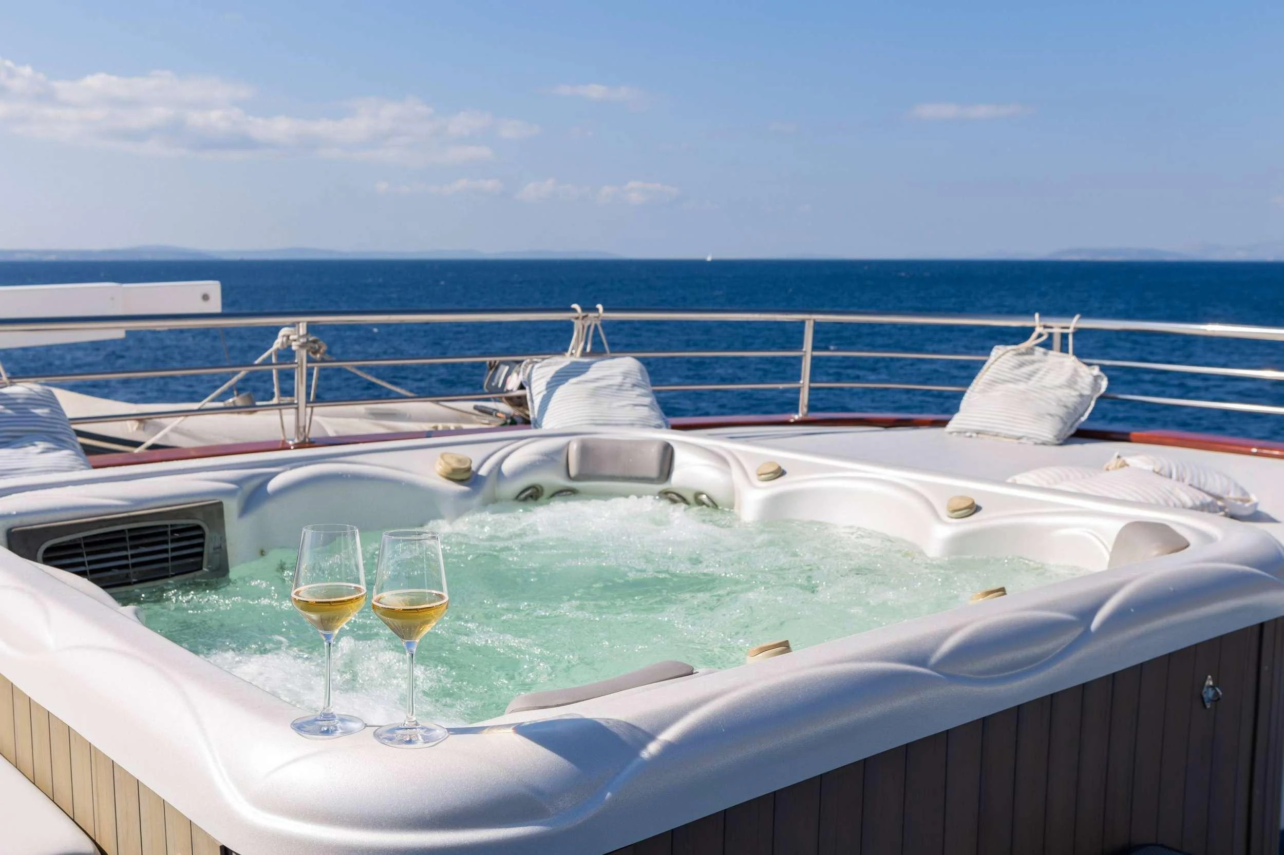 a boat with wine glasses and a bottle on a railing with water and blue sky in the background aboard AMALIA Yacht for Charter