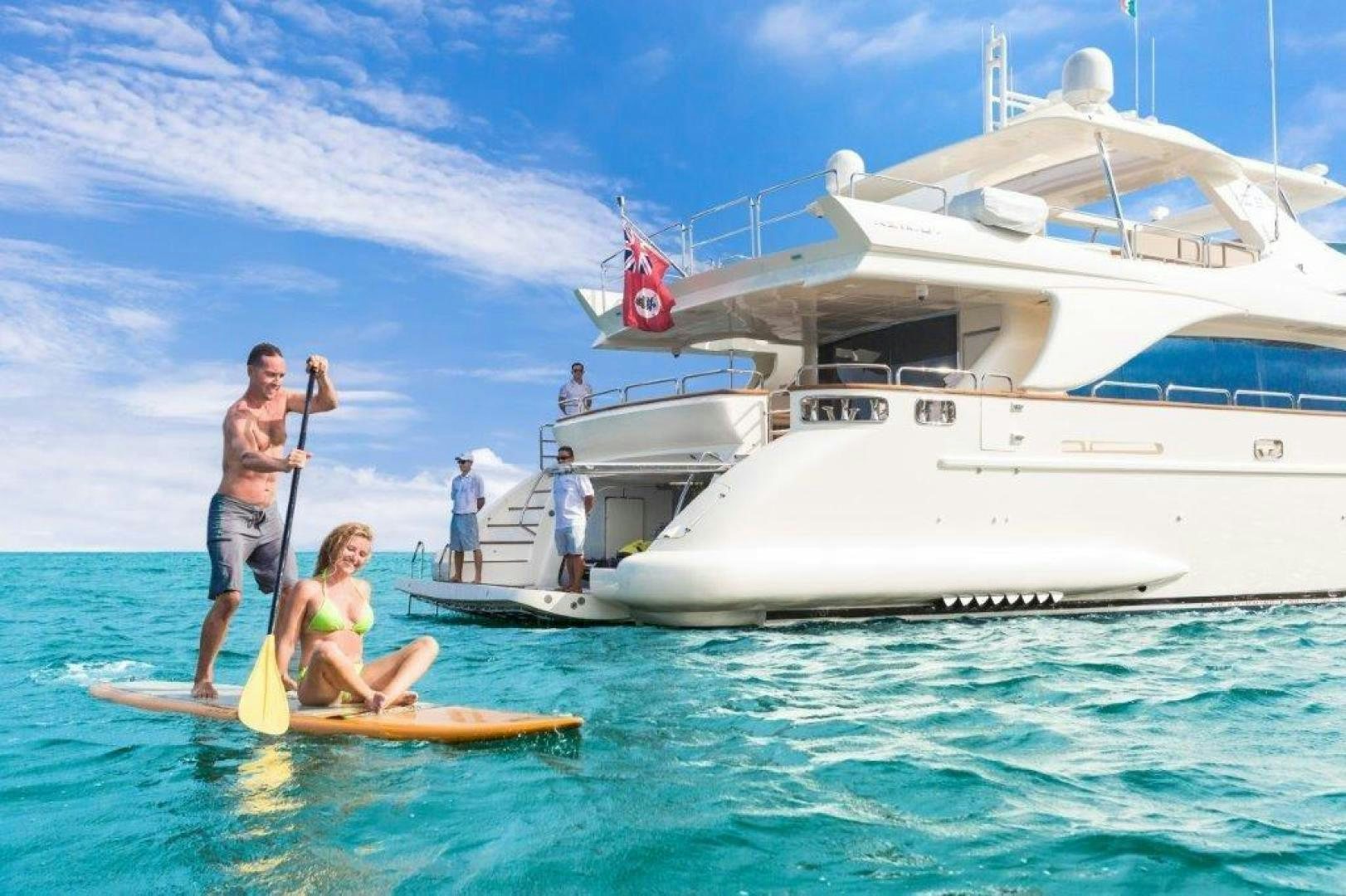 a man and woman on a paddle board in front of a white boat aboard AMANECER Yacht for Sale