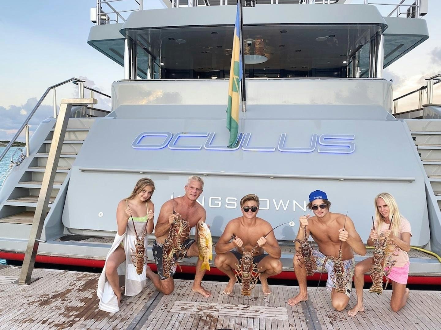 a group of people posing for a photo in front of a boat aboard OCULUS Yacht for Sale