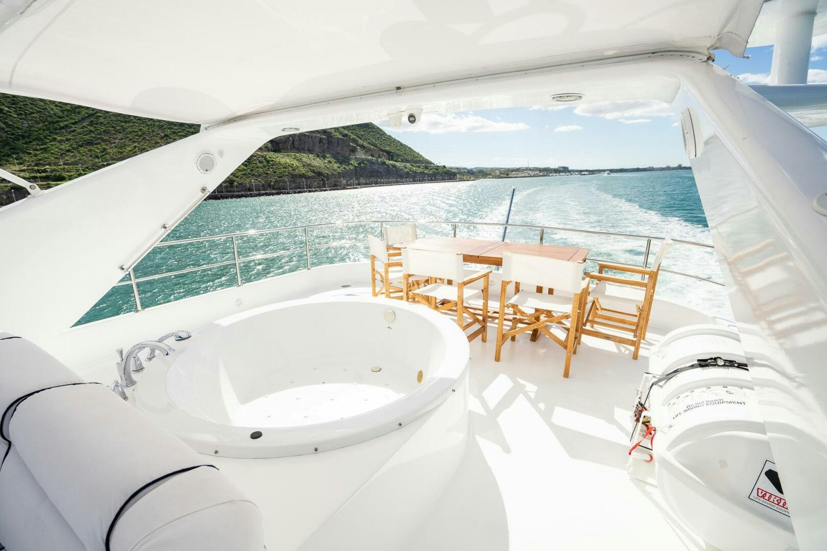 a large white bathtub with chairs and a table and chairs on a beach with a mountain and aboard PURA VIDA  Yacht for Sale