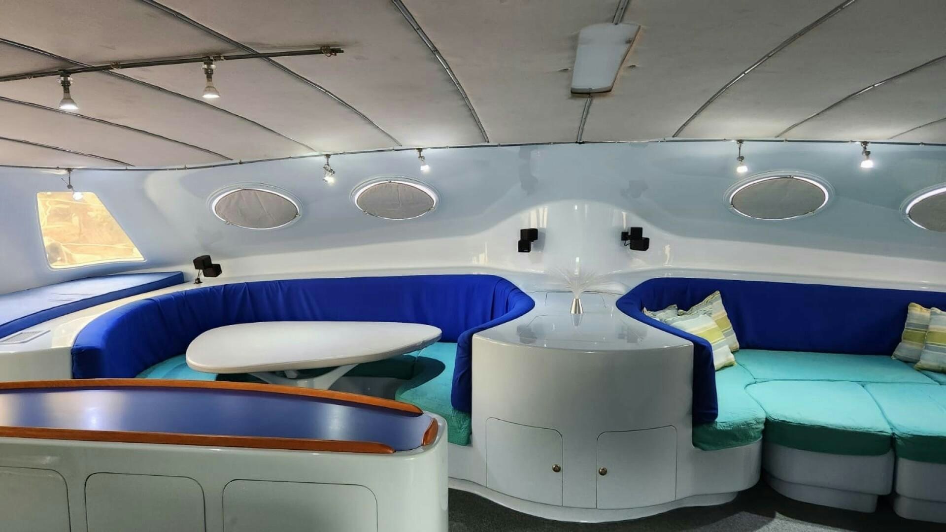 a room with a row of blue seats and a white table aboard FAT CAT Yacht for Sale