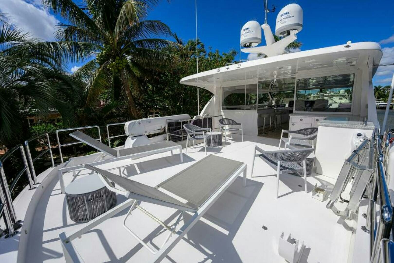 a white lounge chair on a white deck with a white building and palm trees and blue sky with aboard JOURNEY Yacht for Sale