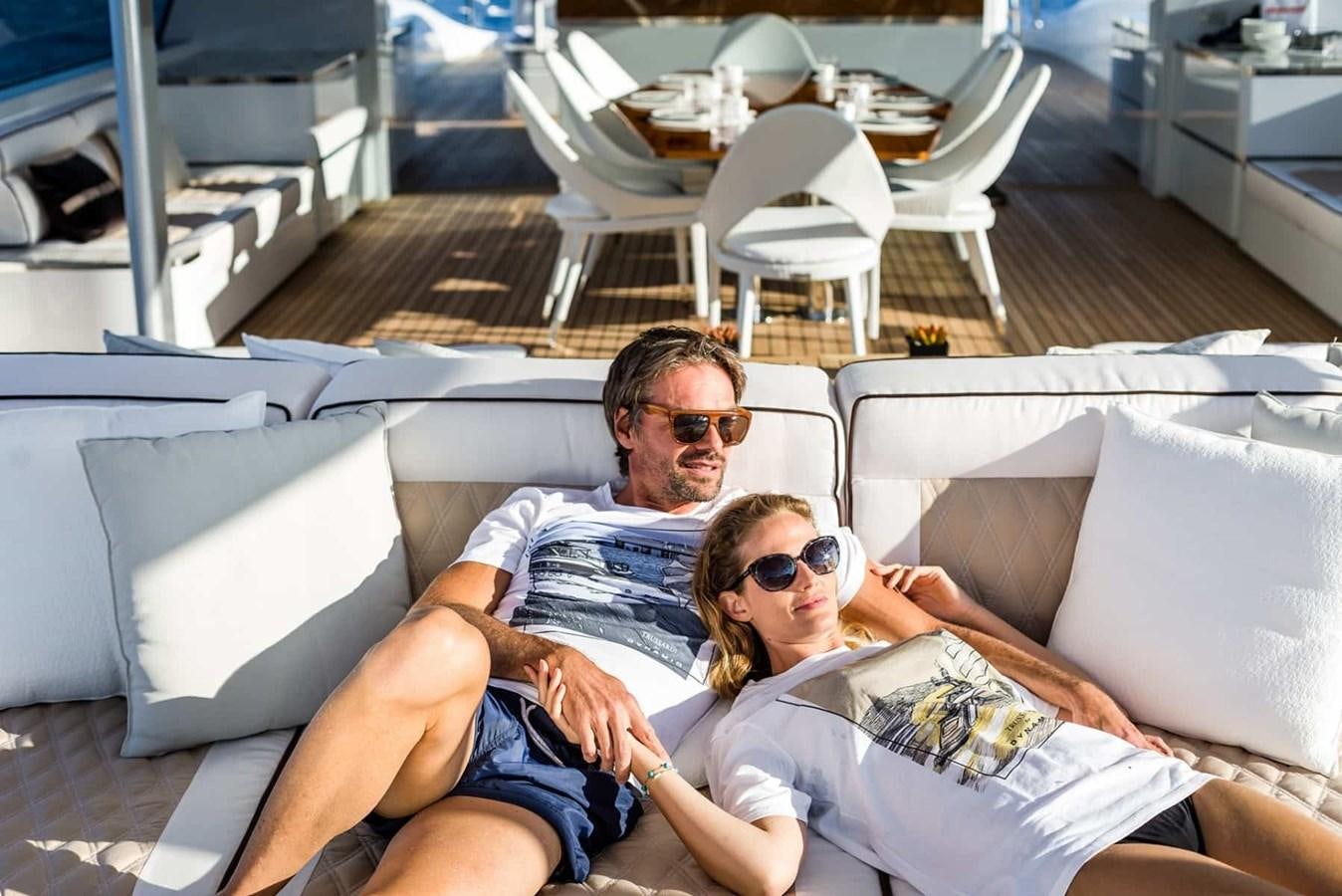 a man and woman sitting on a couch with a laptop aboard GTT 130 Yacht for Sale