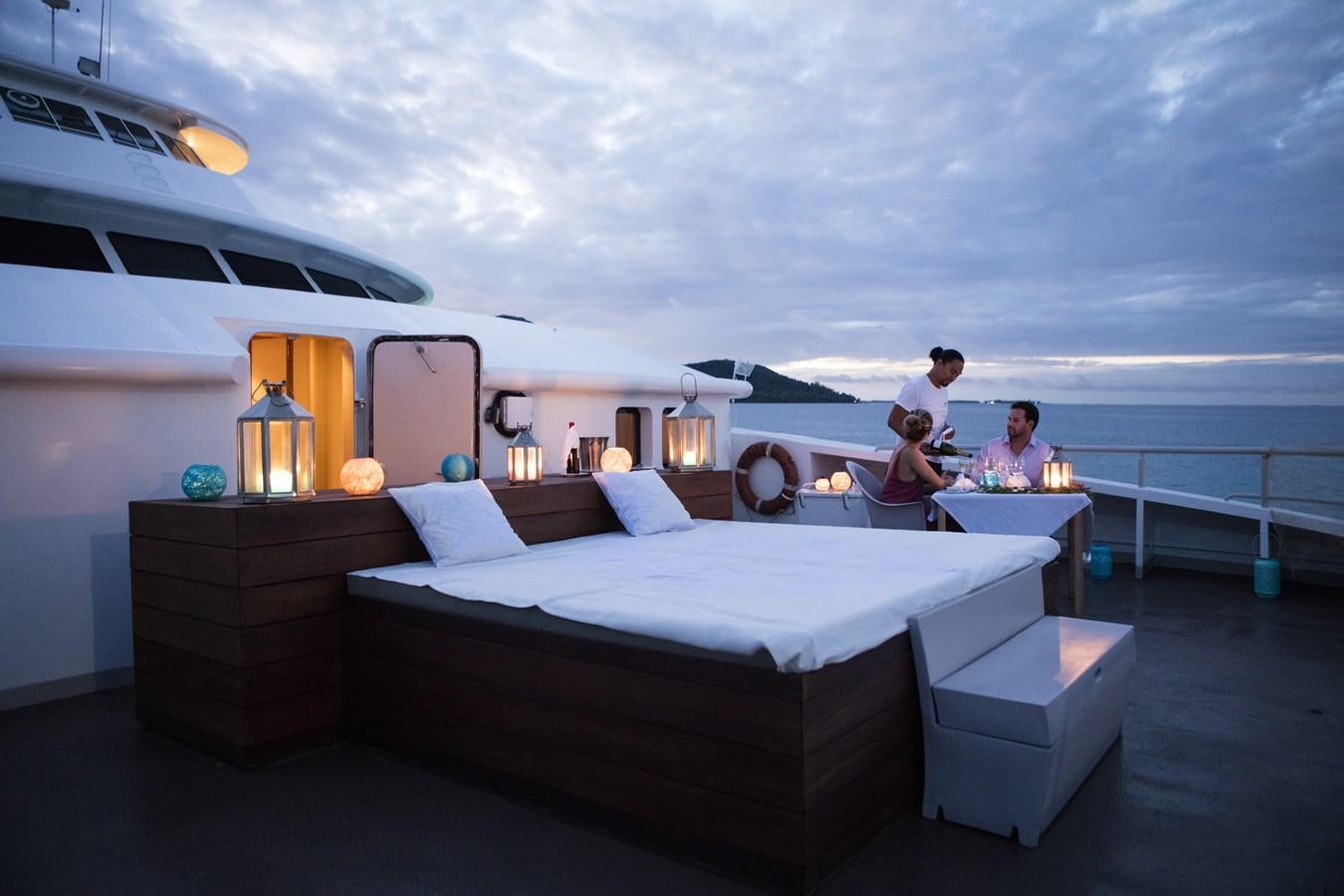 a couple of people sitting on a bed in a room with a large white bed and a large aboard HAUMANA Yacht for Sale