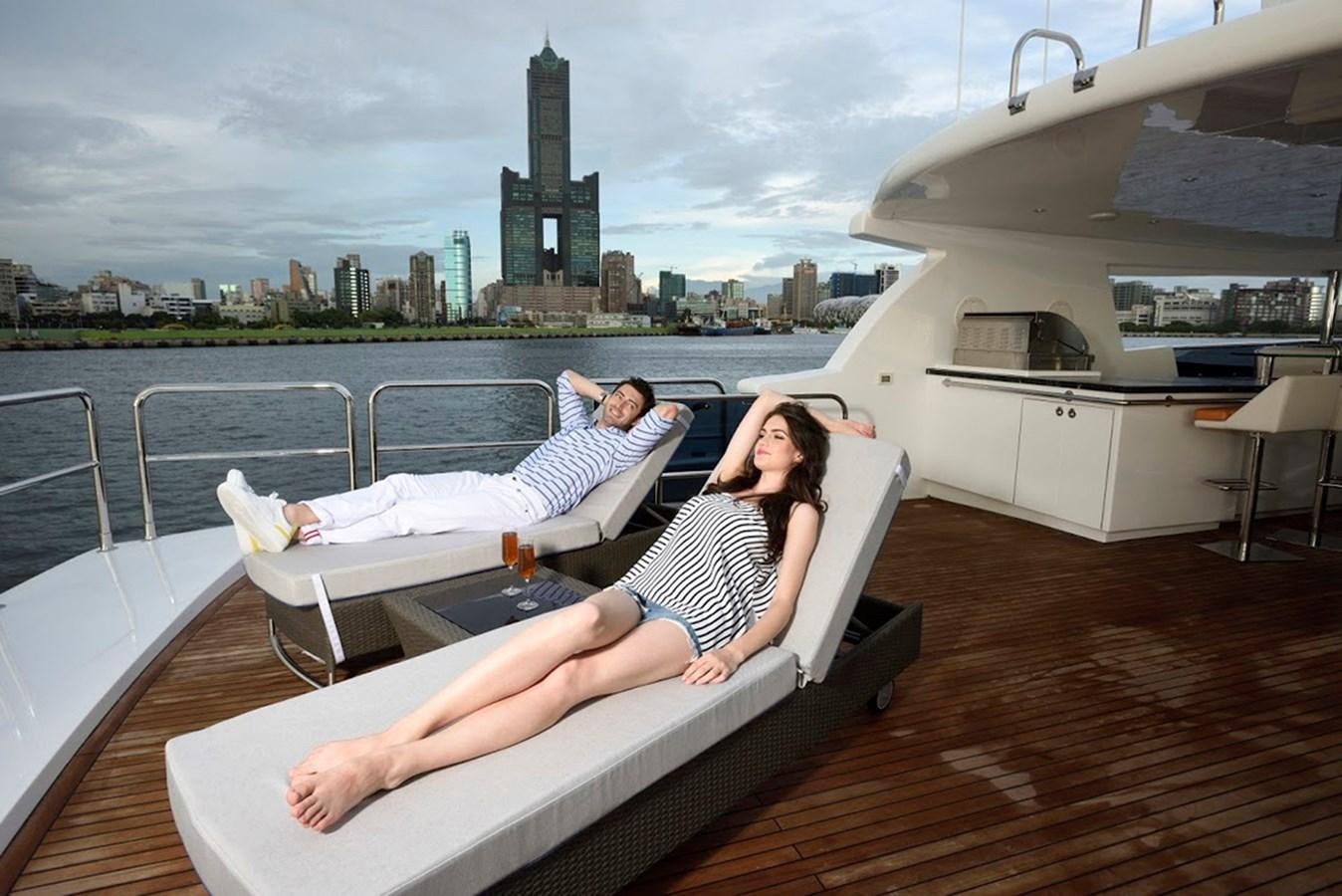 a person lying on a lounge chair on a deck with a city in the background aboard DUMB ASS Yacht for Sale
