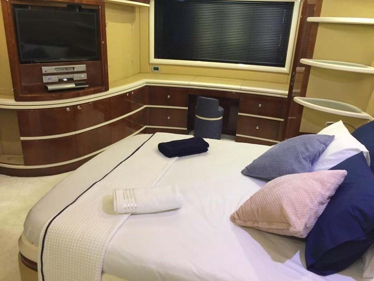 a bed with a television and a table with a pillow and a book aboard AEGINA Yacht for Sale