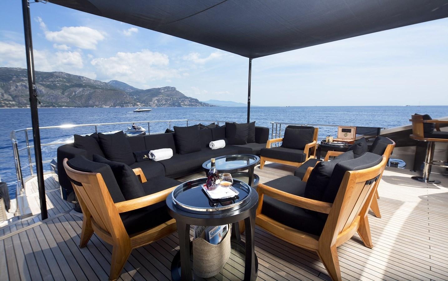 a large living room with a large body of water and mountains in the background aboard DEFIANT Yacht for Sale