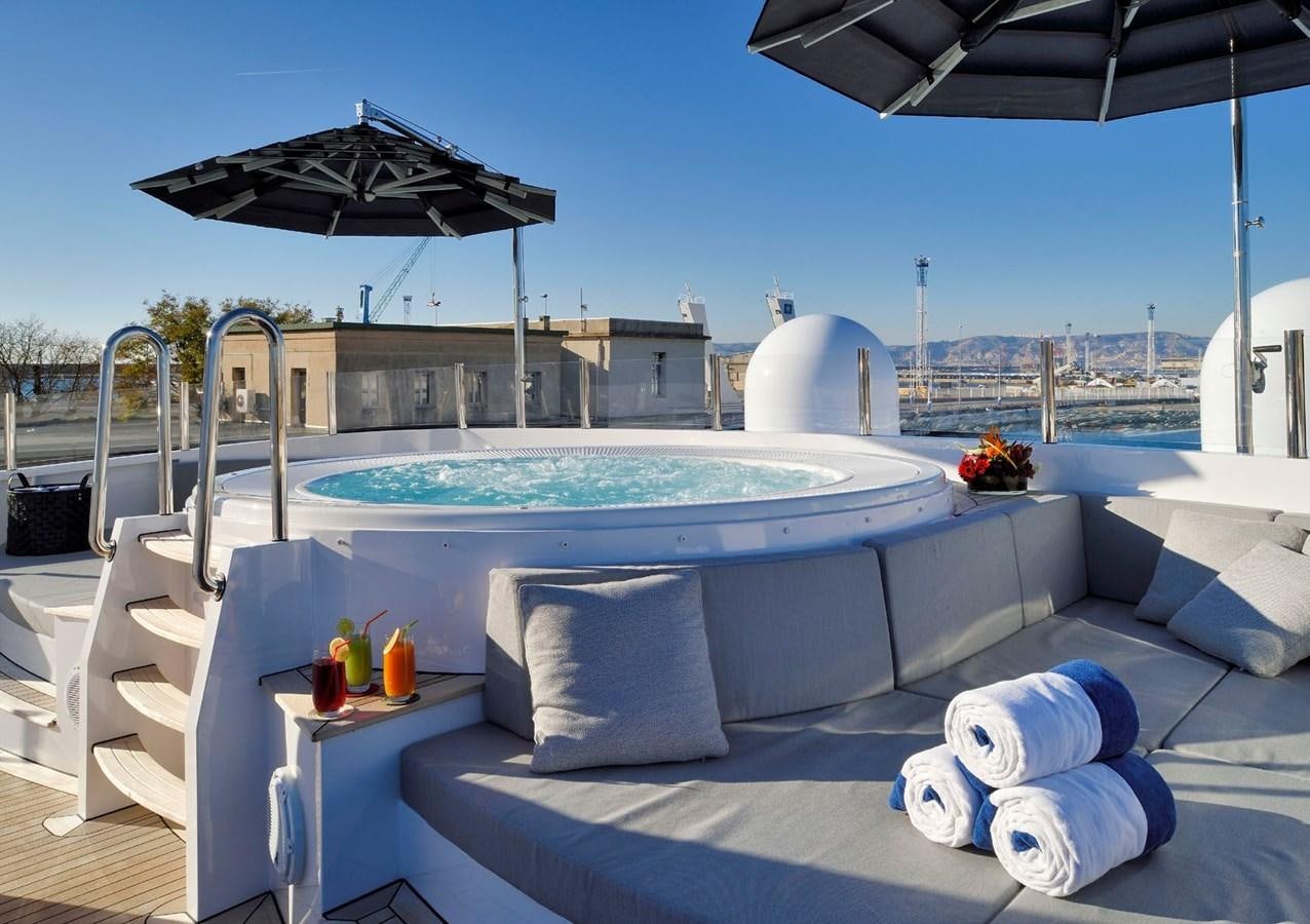 a pool with a large white lounge chair and a large umbrella on a sunny day aboard SANOO Yacht for Sale