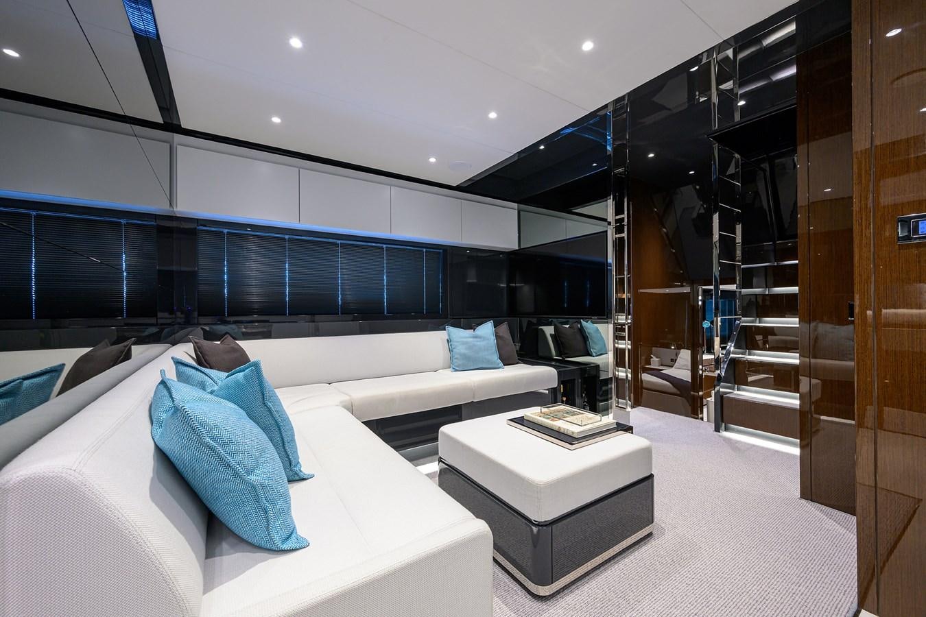 a room with a white couch and a large glass wall with a black shelving unit and a aboard JACQPOT Yacht for Sale