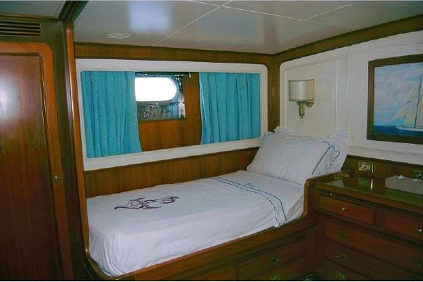 a bed with a white sheet and a blue curtain aboard PATRA Yacht for Sale