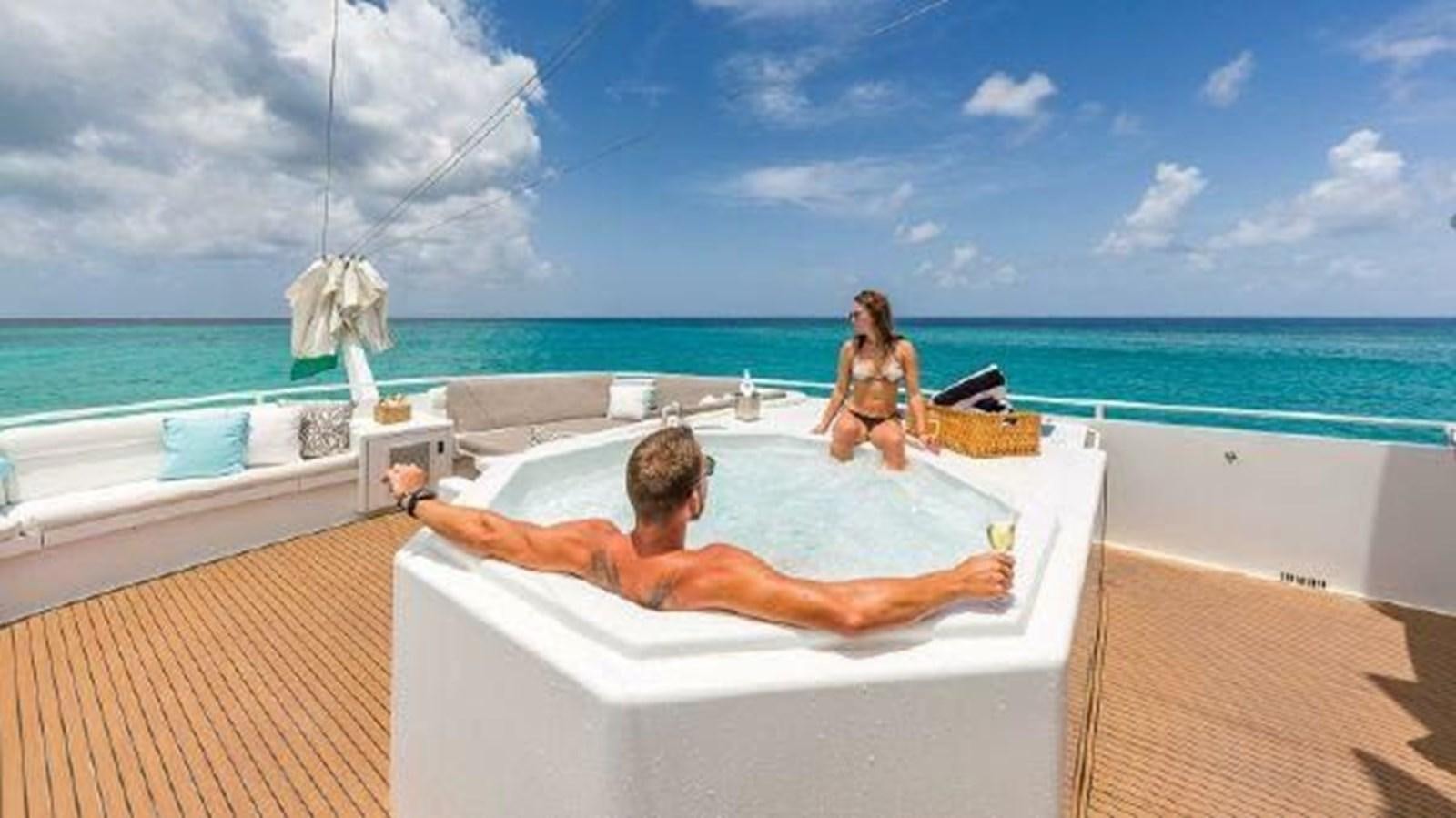 a man lying on a lounge chair on a beach with a woman sitting on the beach and water aboard ROGUE Yacht for Sale