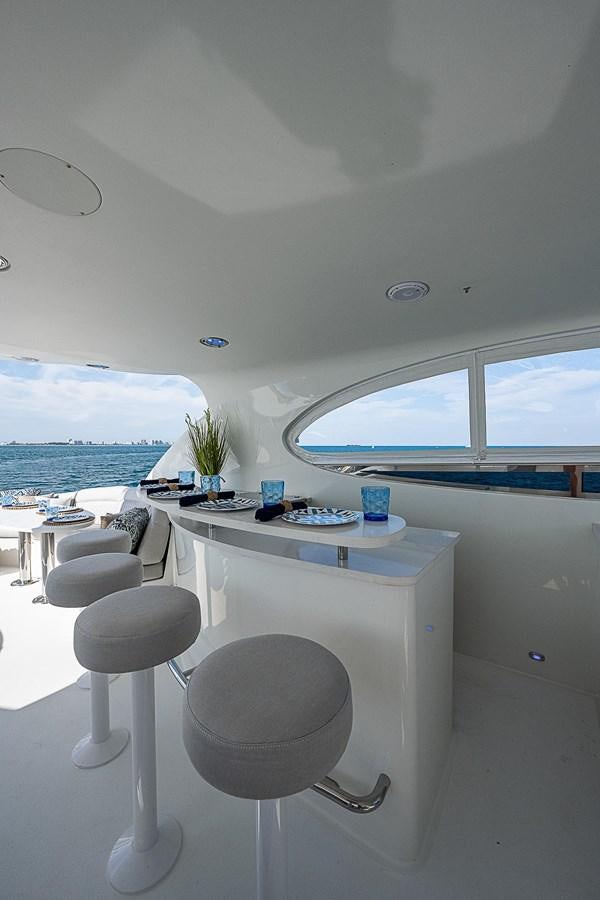 a white table with stools and a window with a view of the ocean aboard LAZZARA 116 OPEN BRIDGE Yacht for Sale