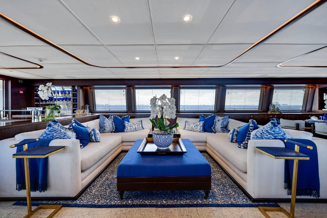 a living room with a blue couch and a table aboard MOONEN ROYAL DENSHIP 120 Yacht for Sale