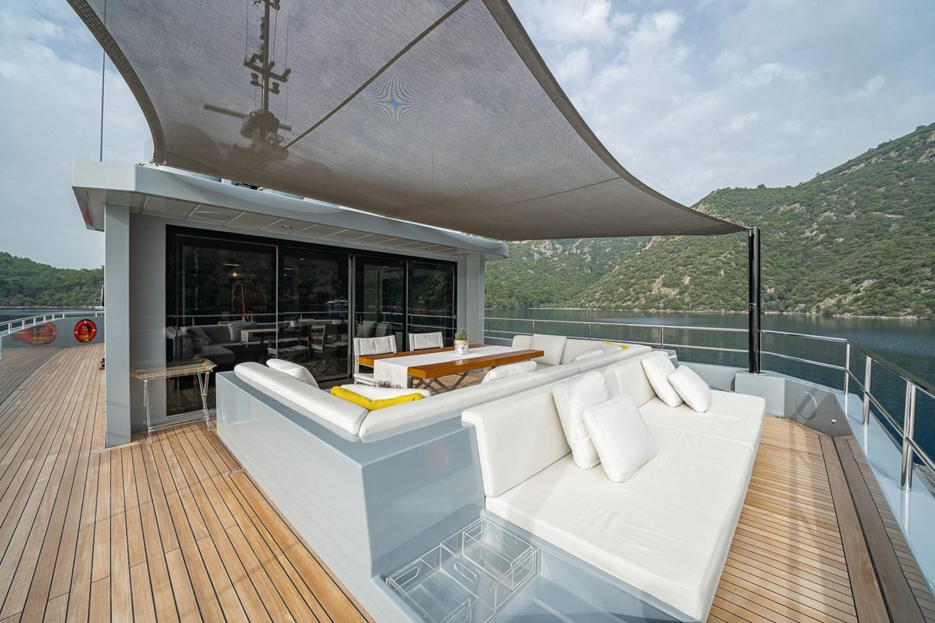 a large white lounge chair on a deck with a view of a mountain range and trees aboard ESOSH Yacht for Sale