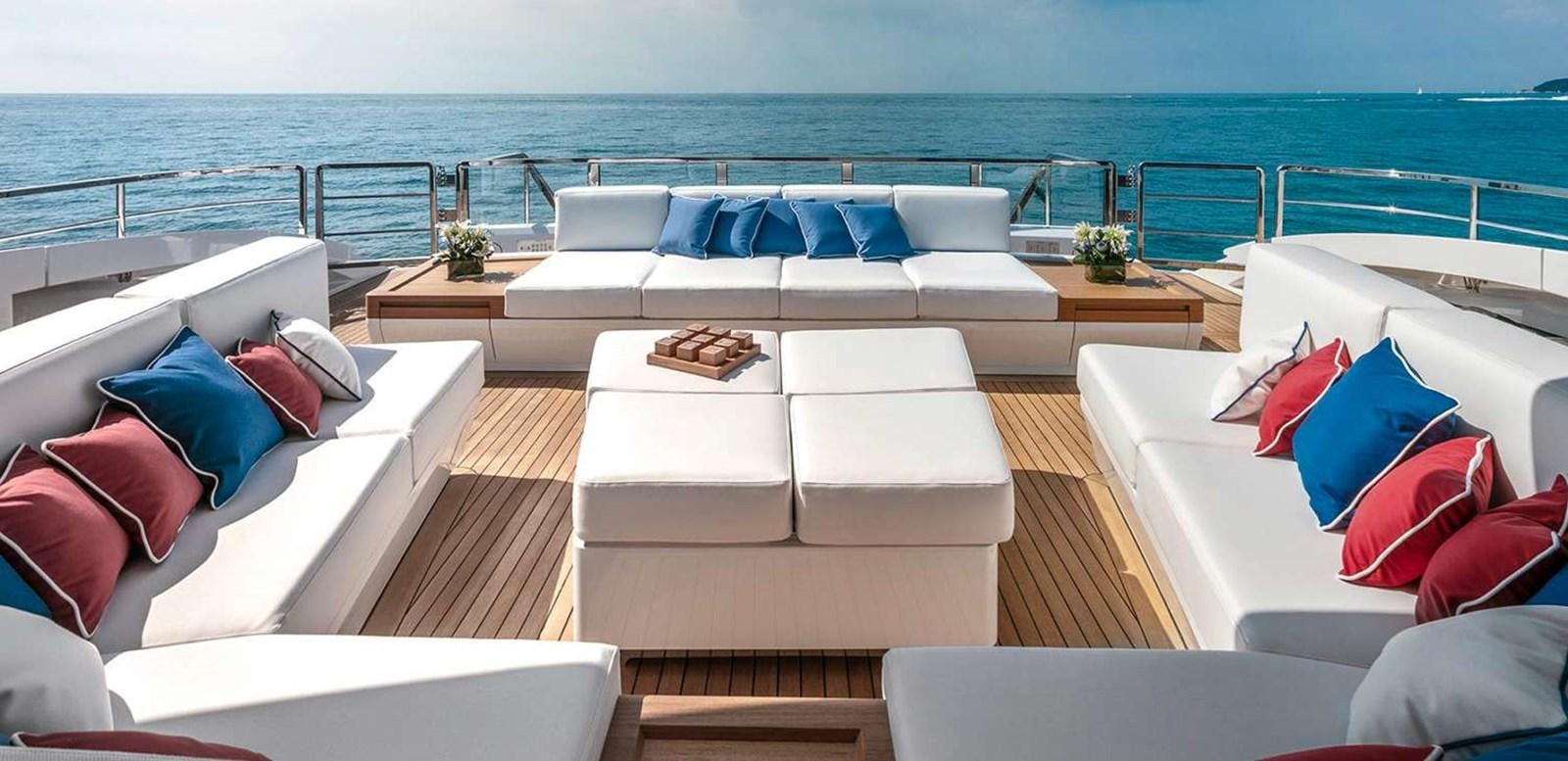 a room with a couch and a table with pillows and a large body of water in the background aboard EL LEON Yacht for Sale