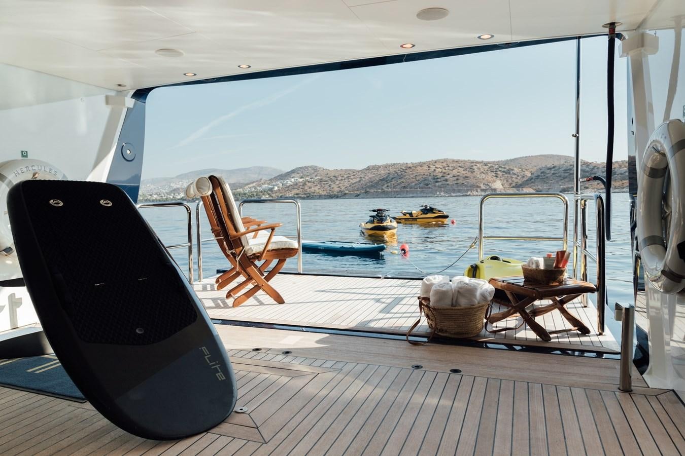 a deck with a chair and a table on it and boats in the water aboard HERCULES Yacht for Sale