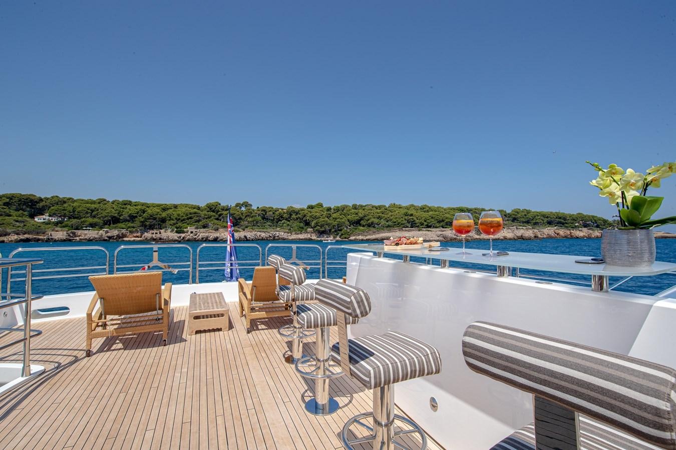a deck with chairs and tables on it by a pool with trees in the background aboard KING OF OIL Yacht for Sale
