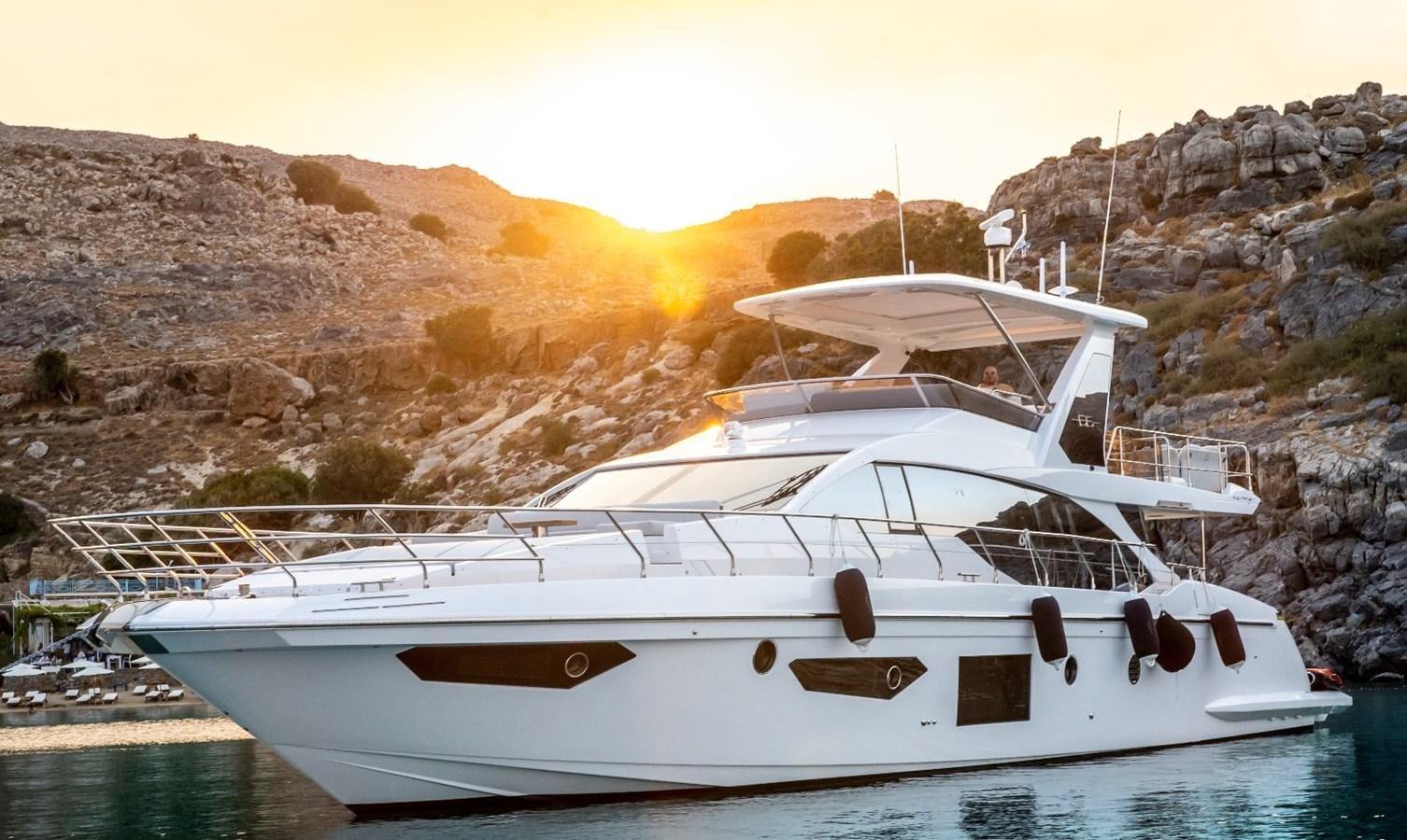 a white boat on a body of water with a hill in the background aboard ATLANTIS OF LONDON Yacht for Sale