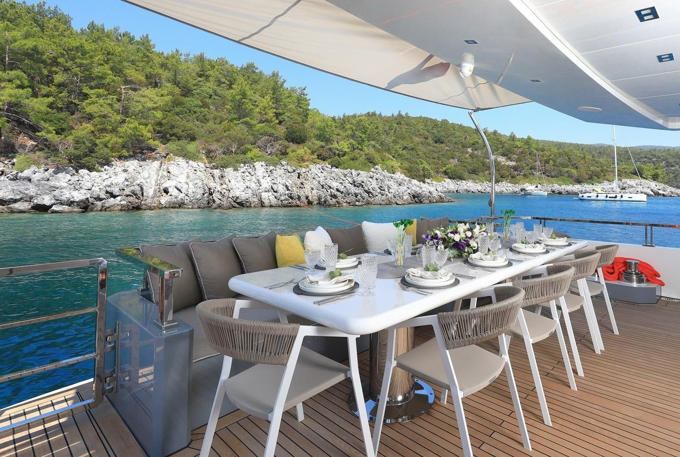 a table set for a meal on a balcony overlooking a body of water aboard TORTURA Yacht for Sale