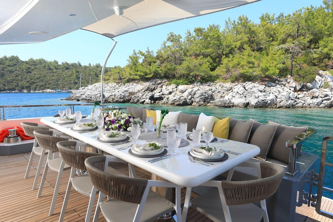 a table set for a meal on a patio with a body of water and trees in the background aboard TORTURA Yacht for Sale