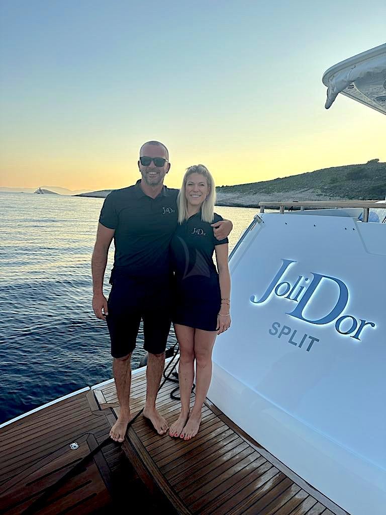 a man and woman standing on a dock by water aboard JOLIDOR Yacht for Charter